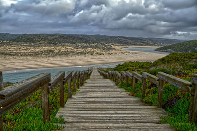 Wooden walkway leading towards sea against sky