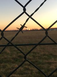 Close-up of chainlink fence against sky during sunset