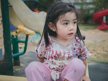 Cute girl looking away while sitting at playground 