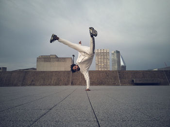 Portrait of young man doing handstand on building terrace against cloudy sky