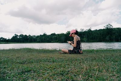 Side view of woman sitting on land against sky