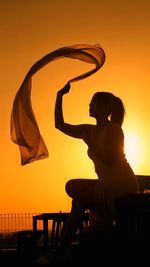 Woman sitting against orange sky during sunset