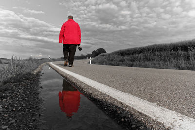 Rear view of woman walking on road against cloudy sky