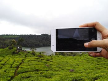 Man photographing with mobile phone against sky
