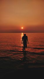 Silhouette woman walking at beach against sky during sunset