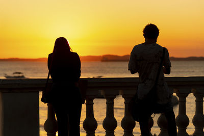 Silhouette people looking at sea against sky during sunset