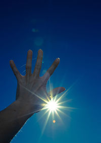 Cropped image of hand against sun shining in sky