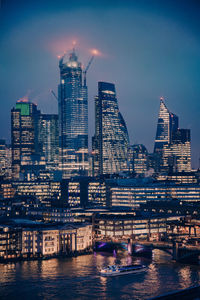 Modern illuminated buildings by river against sky in city at night