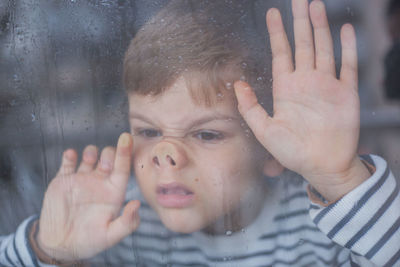 Portrait of boy looking through wet window