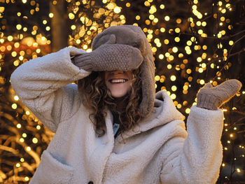 Portrait of young woman standing against illuminated christmas tree