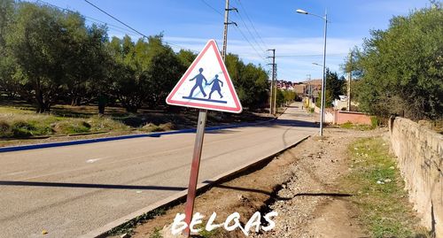 Road sign by street in city against sky