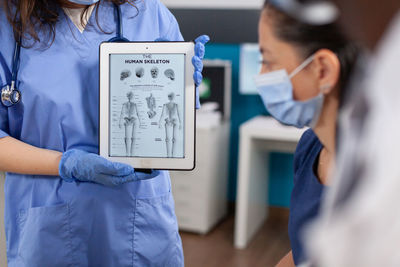 Midsection of nurse showing digital tablet to patient