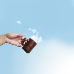 Cropped hand holding mug against cloudy sky