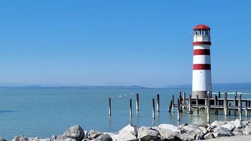 Lighthouse by sea against clear sky