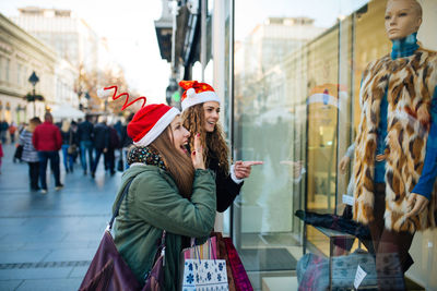 Surprised young friends pointing window display of store in city