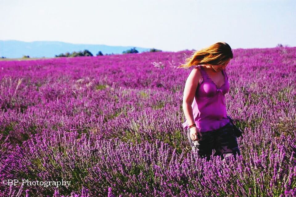 WOMAN STANDING ON GRASSY FIELD AGAINST SKY