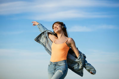 Cheerful young woman standing against sky