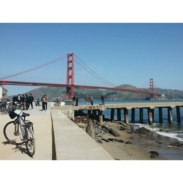 bridge - man made structure, connection, built structure, architecture, clear sky, bridge, engineering, suspension bridge, transportation, water, men, transfer print, lifestyles, leisure activity, copy space, river, walking, person, large group of people