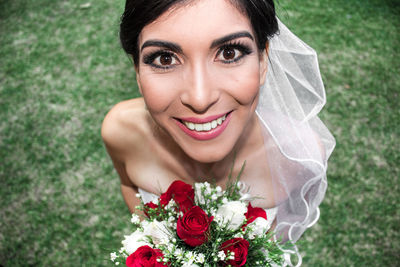 Portrait of smiling bride with bouquet standing on grass
