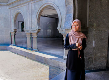 Woman in hijab holding counting rosary beads while praying at mosque