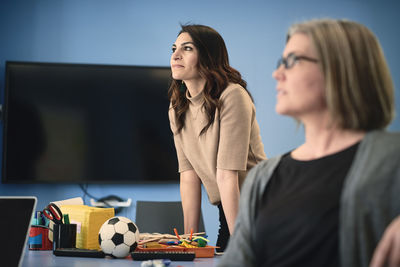 Mature female engineer looking away while standing by colleague at table in office