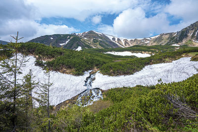 Stream of water flowing with snow covered from both sides on slope of hill