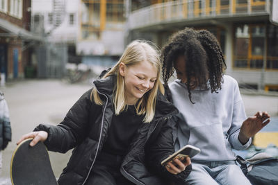 Happy girls showing smart phone to friend at school campus