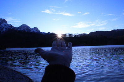 Woman hand by lake against sky