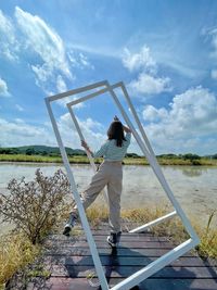 Low angle view of woman sitting on swing at beach against sky