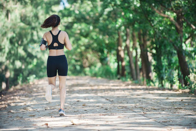 Full length rear view of young woman jogging on road amidst trees