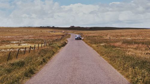 Scenic view of road amidst field against sky