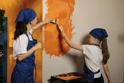 Rear view of mother and daughter standing against wall