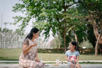 Mother and daughter having food while sitting at park