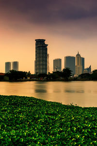 Scenic view of river by buildings against sky during sunset