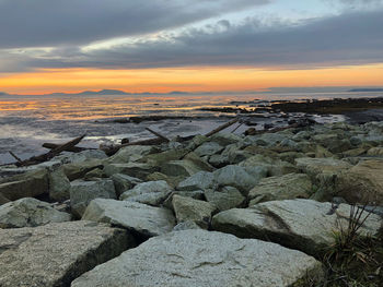 Rocks on beach against sky during sunset