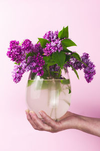 Close-up of hand holding purple flower vase against white background