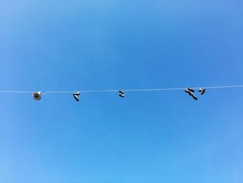 Low angle view of shoes hanging on cable against blue sky