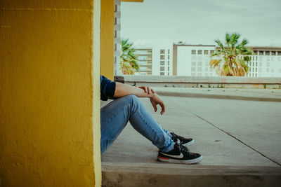 Full length of young woman sitting on wall against building