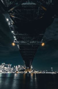 Bridge over river by illuminated city at night