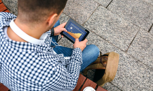 High angle view of man using digital tablet while sitting on bench