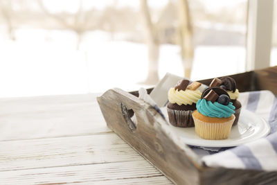 Tasty multicolored muffins and cupcakes on the white plate on a wooden tray with towel