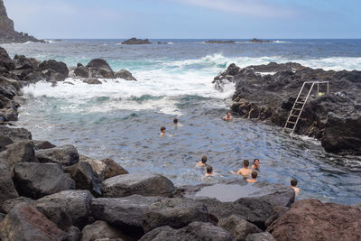 People swimming in natural volcanic thermal sea pool in ponta da ferraria, sao miguel island, azores