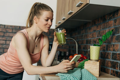 Sportswoman drinking vegan smoothie made of green vegetables and celery in the kitchen 