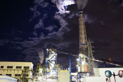 Low angle view of illuminated factory against sky at night