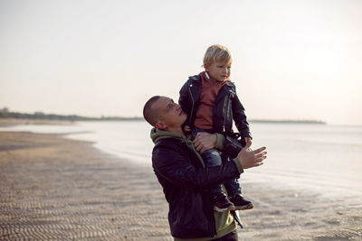 Father and son in leather jackets in autumn walking in nature near the bay on the beach with sand