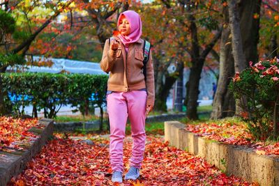 Full length of young woman standing by trees during autumn