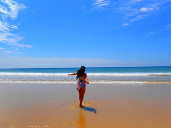 Rear view of woman standing at beach against sky