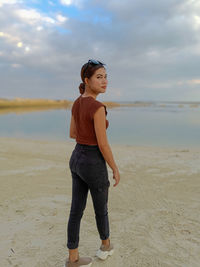 Side view of young woman standing at beach against sky