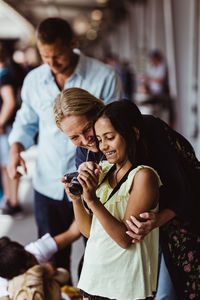 Happy mother and daughter looking at camera while standing by family at train station