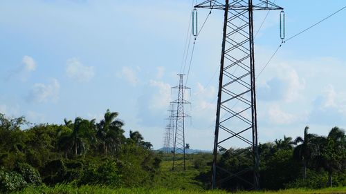 Electricity pylons on grassy field amidst trees against sky
